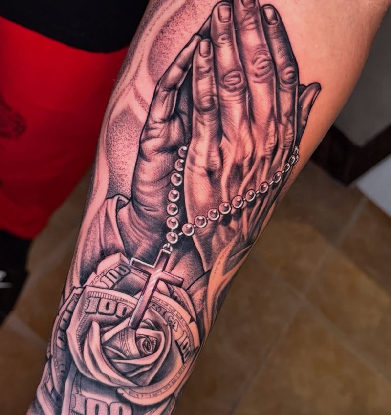 Black and grey praying hands with a rosary and a rose made of hundred-dollar bills
